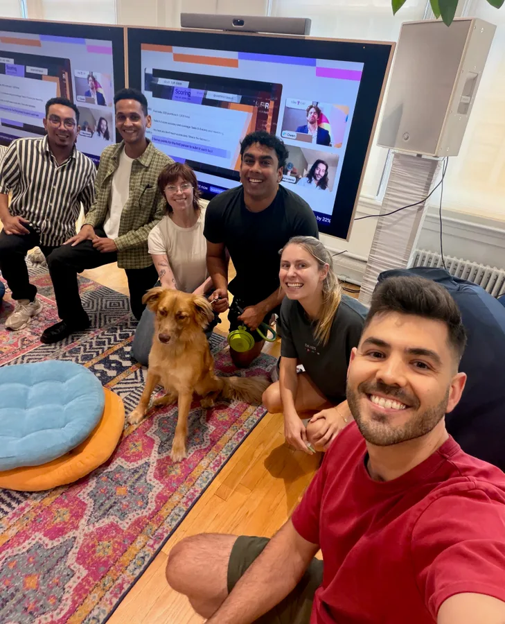 The Clay ecosystem team and office dog gathered in front of screens showing Clay Cup